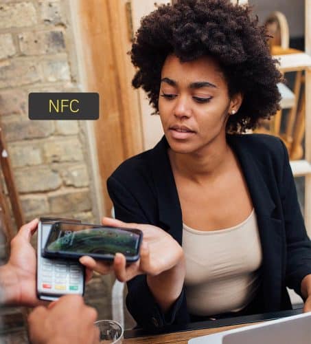 A woman at a restaurant uses her smartphone to pay for her meal by tapping her phone against a credit card reader.