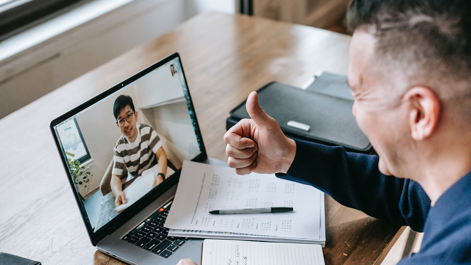 Two men communicating over video conference. One giving a thumbs up gesture.